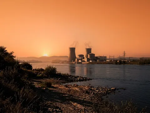 Une centrale nucléaire au bord d'un fleuve à l'étiage, sous un ciel orange de canicule.