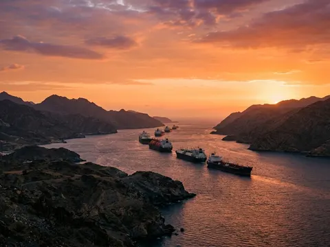 Un détroit étroit entre deux côtes désertiques au coucher du soleil, une file de méthaniers et de pétroliers sur l'eau.