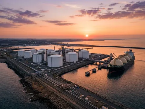 Vue aérienne d'un terminal méthanier au coucher du soleil, réservoirs cylindriques alignés et méthanier à quai.
